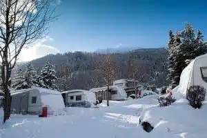 Schneebedeckte Caravans auf Stellplätzen von Camping Sölden mit Blick auf bewalldete Berge