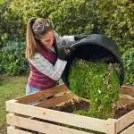 Frau entleert Korb mit Rasenschnitt auf Komposthaufen