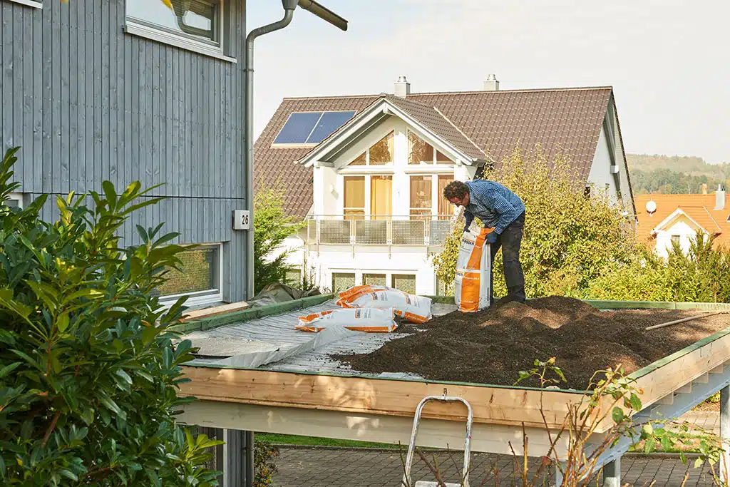Mann verteilt Erde auf einem Carport-Dach