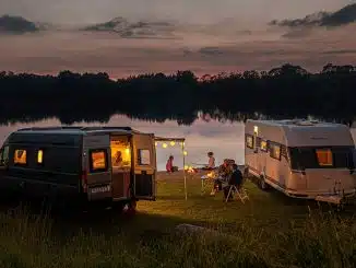 Ein Wohnwagen und ein Wohnmobil mit Campern am Seeufer bei Sonnenuntergang