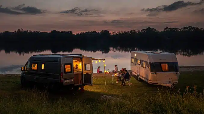Ein Wohnwagen und ein Wohnmobil mit Campern am Seeufer bei Sonnenuntergang
