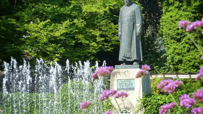 Kneipp-Statue neben einem Brunnen und Blumen