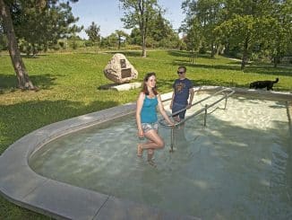 Kneipp-Campingplatz werden: Eine Frau und ein Mann beim Wassertreten in einem flachen Wasserbecken auf einer Wiese