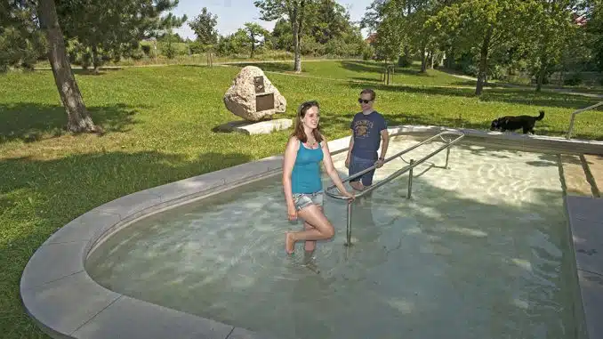 Kneipp-Campingplatz werden: Eine Frau und ein Mann beim Wassertreten in einem flachen Wasserbecken auf einer Wiese