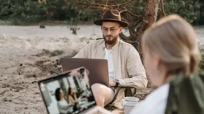 Eine Frau und ein Mann auf Campingstühlen nutzen Laptops draußen
