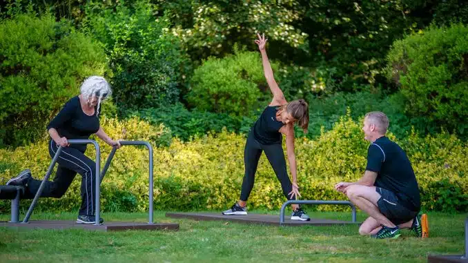 Zwei Frauen trainieren an Outdoor-Fitnessgeräten unter Anleitung eines Trainers