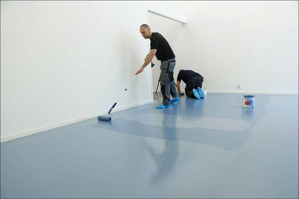 Zwei Männer lackieren einen glatten Fußboden in einer hellblauen Farbe