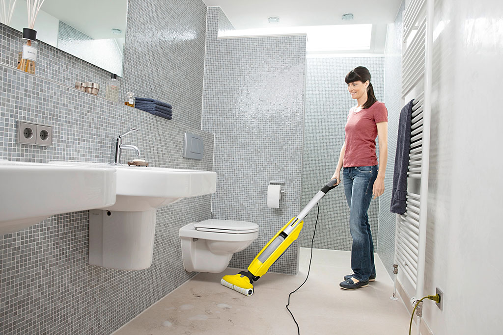 Frau nutzt gelbes Fußboden-Reinigungsgerät auf Badezimmerboden